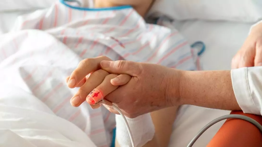 Una persona agafa de la mà a un pacient, imatge de detall, Hospital Sant Joan de Déu