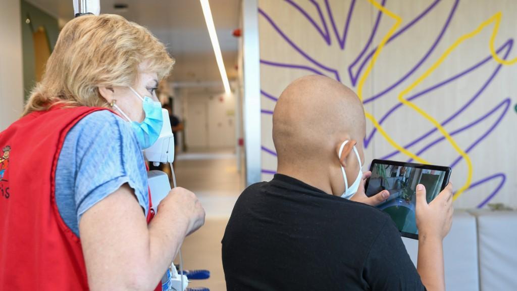 Un paciente del hospital juega a Saurus Kids, con el acompañamiento de una voluntaria del Hospital Sant Joan de Déu Barcelona.