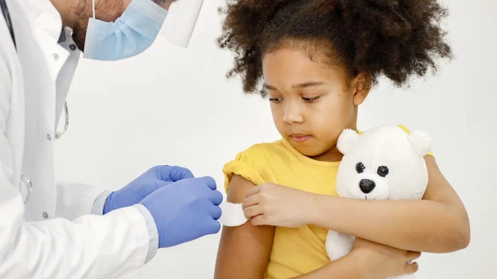 Girl receiving vaccine in arm with teddy bear