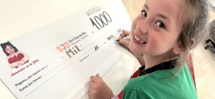Una niña entrega un cheque con una donación en el Hospital Sant Joan de Déu