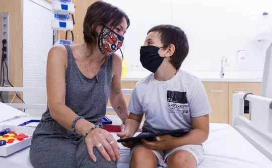 Una madre mira a su hijo en un box del Hospital de día del SJD Pediatric Cancer Center
