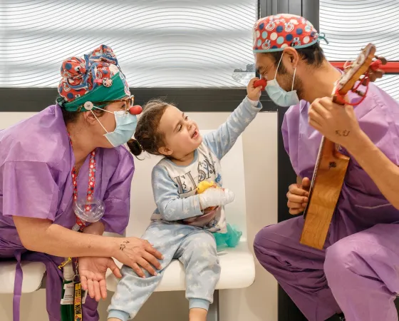 Paciente sonriendo y tocando la nariz a un payaso de Hospital